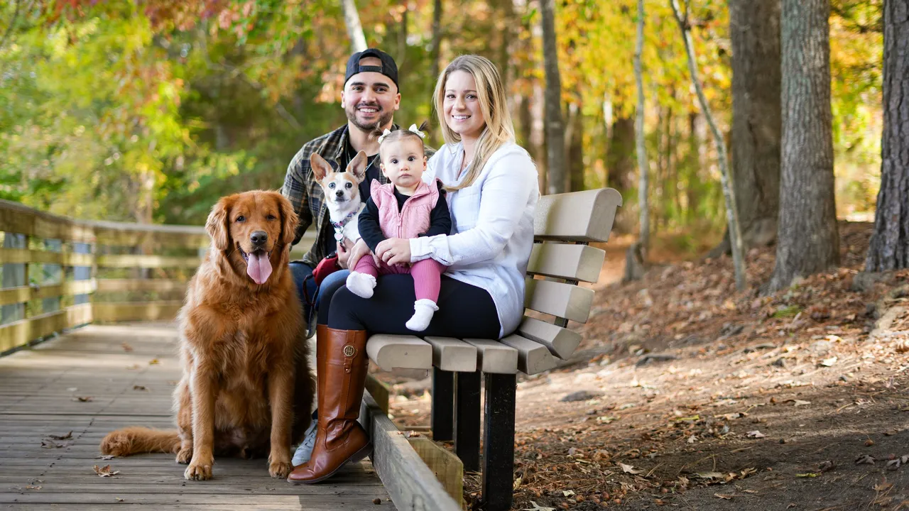 The whole family on a boardwalk bench — Sloan on Ashley's lap, Ella tucked in, and Jax the golden retriever alongside