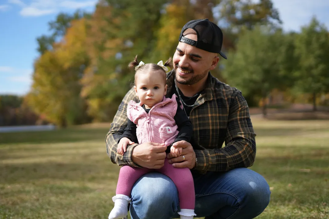 Mario crouched in the park with Sloan on his knee