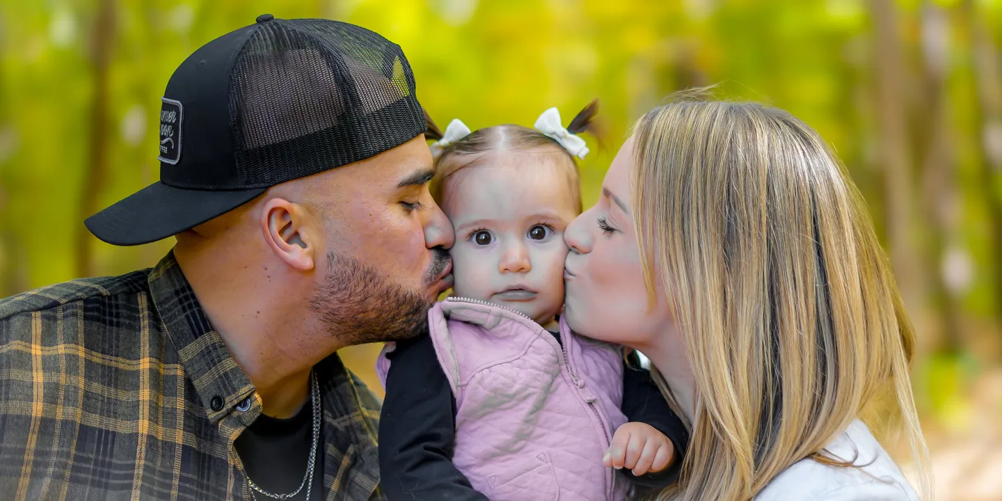 Close-up of Mario and Ashley kissing Sloan's cheeks against golden autumn woods