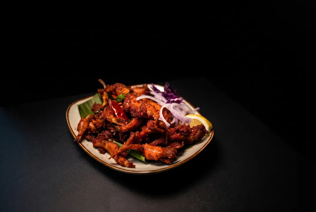 Crisp chicken fry piled high with a dried red chili, pickled onion, red cabbage, and lemon, on black slate under dramatic key light
