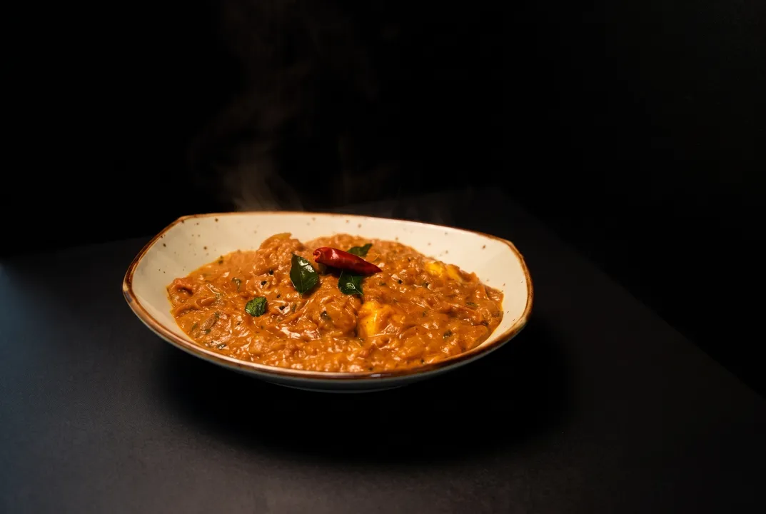Steam rising from a thick curry topped with a dried red chili and curry leaves
