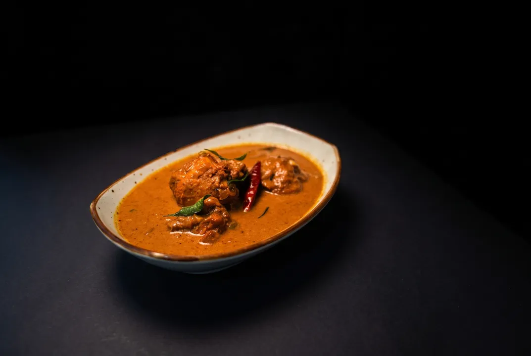 Chicken curry in an oval bowl with a dried red chili and curry leaves