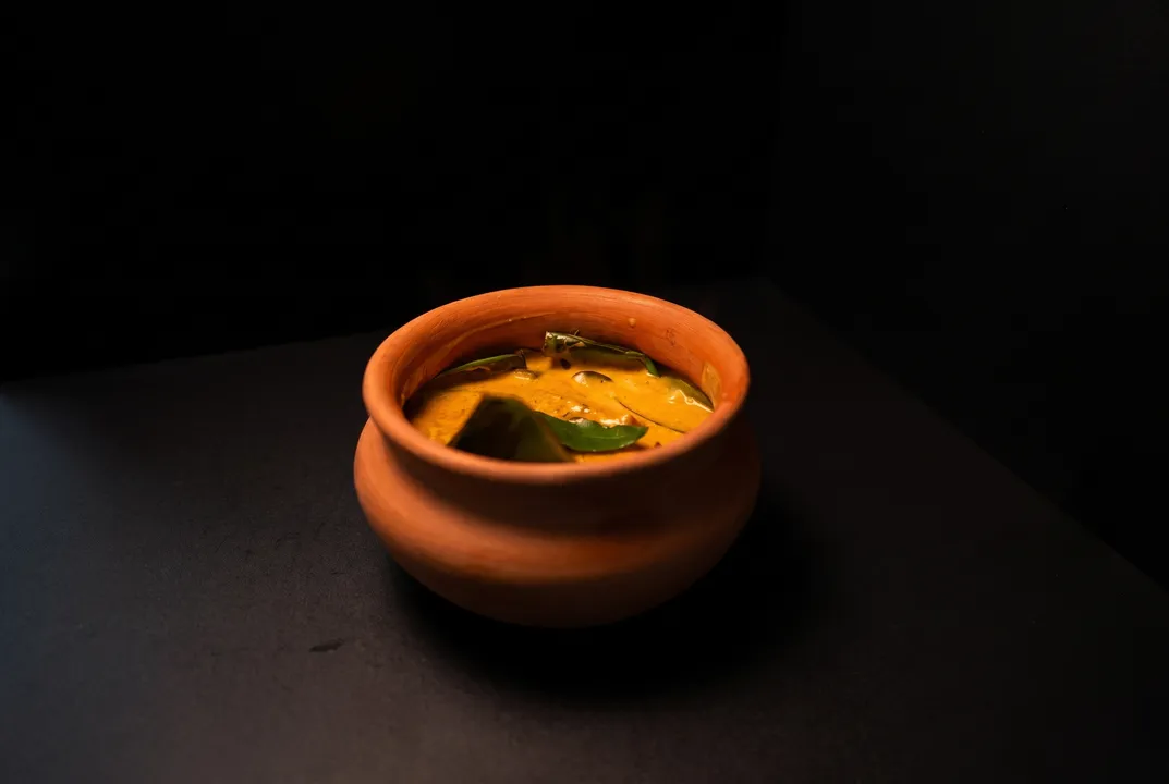 Kerala fish curry in a terracotta clay pot, glowing against the dark frame