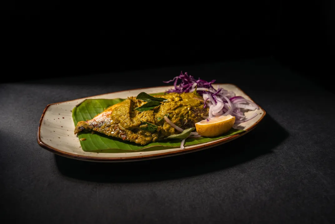 Whole fish in green masala on a banana leaf with pickled onion and lemon