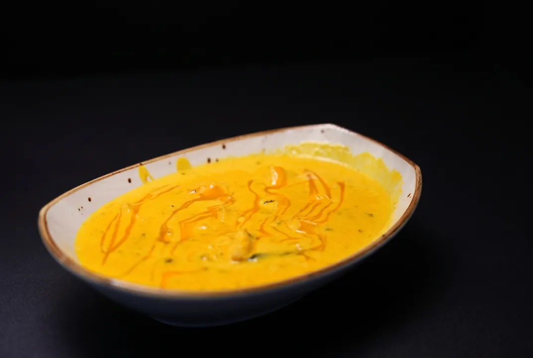 A golden curry with a chili-oil drizzle in a speckled ceramic bowl