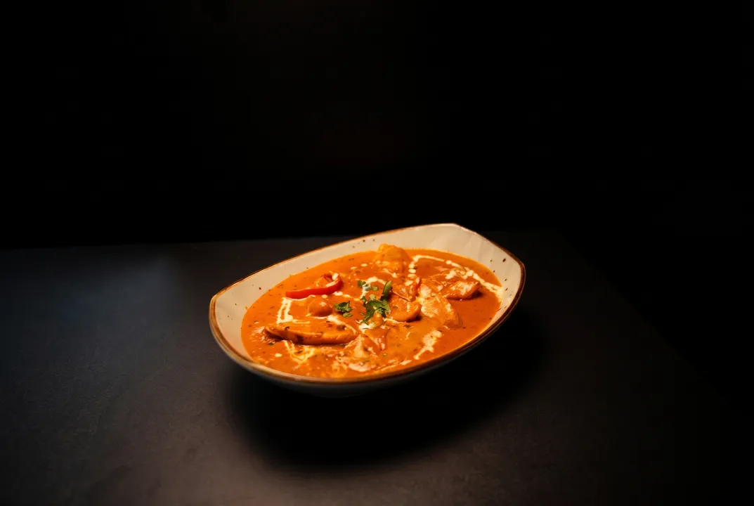 Butter chicken with a cream swirl, red pepper, and cilantro in a speckled bowl