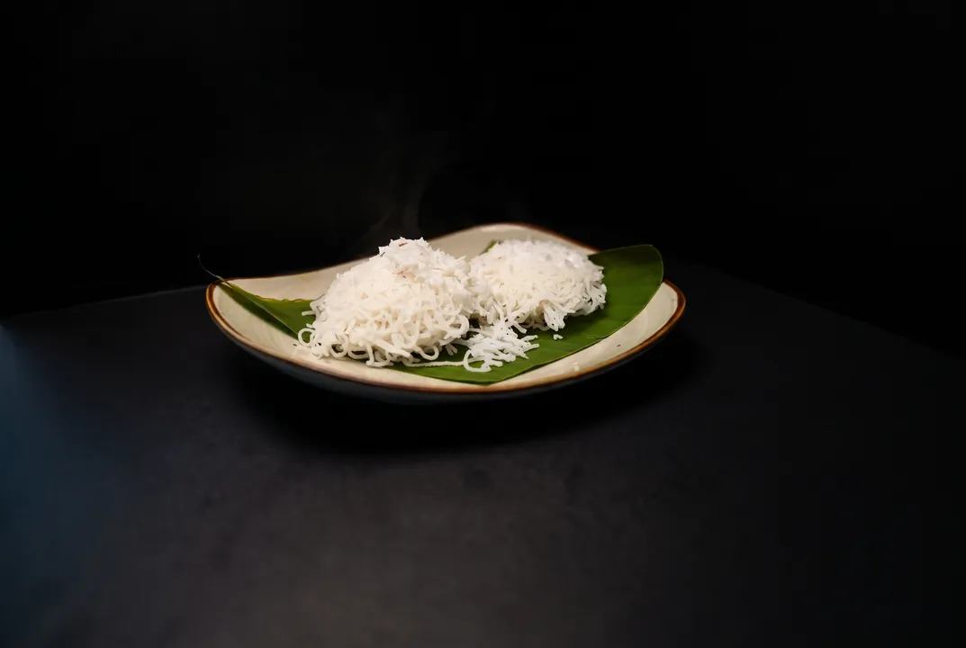 Steaming idiyappam string hoppers with grated coconut on a banana leaf