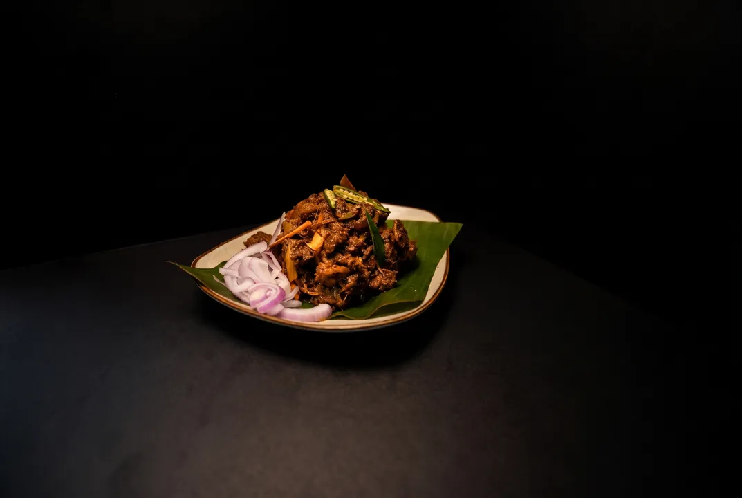 Beef dry roast mounded on a banana leaf with onion rings and green chili