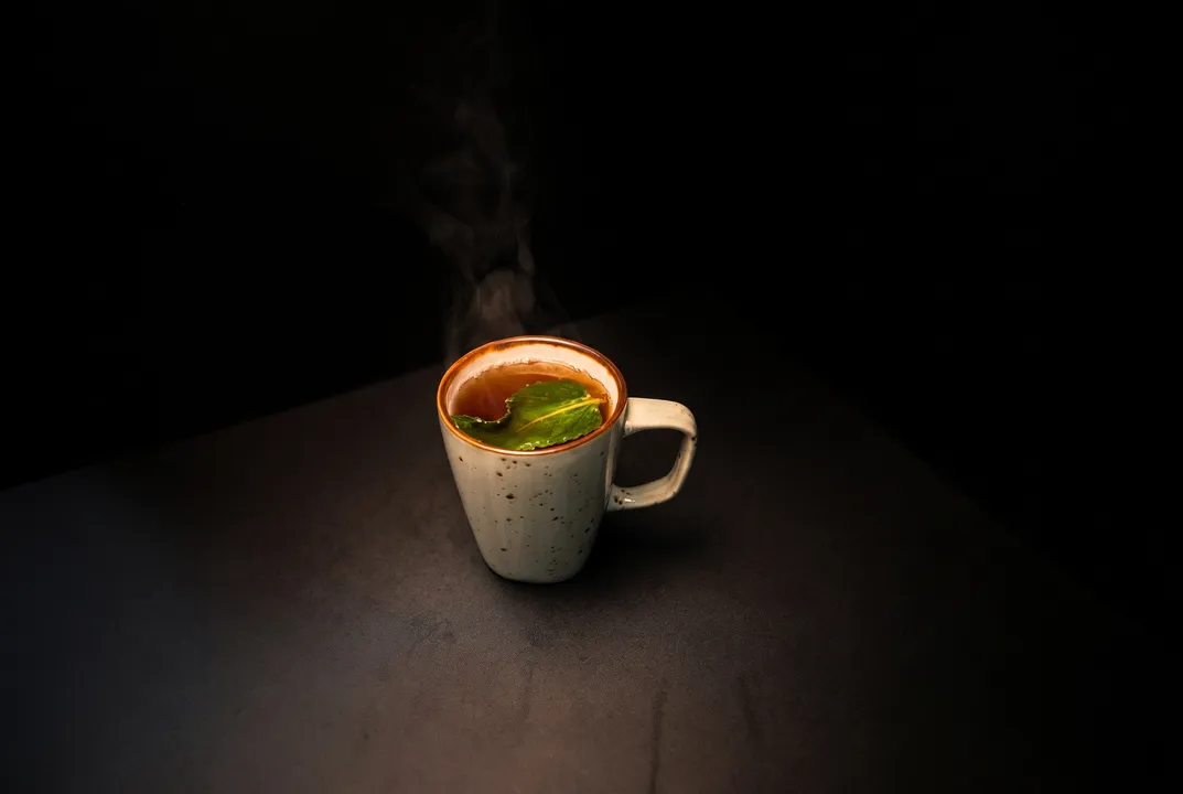 A steaming speckled mug of chai with a fresh leaf, lit like a portrait