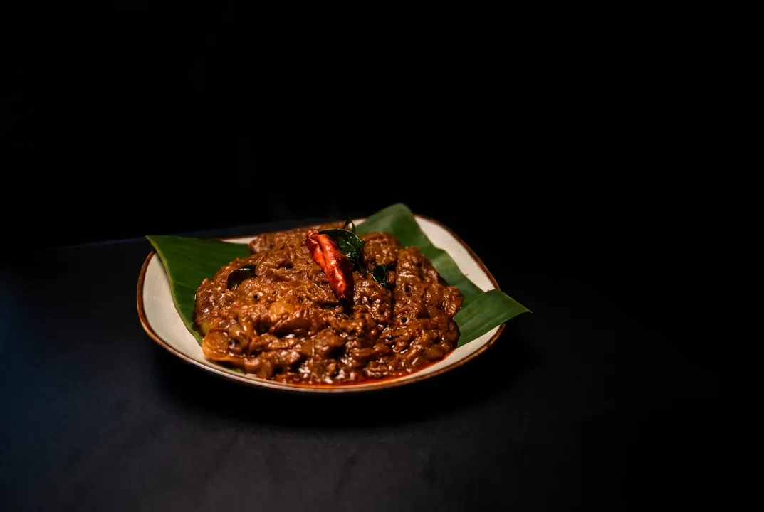 Slow-roasted dark beef curry topped with a dried red chili, served on a banana leaf